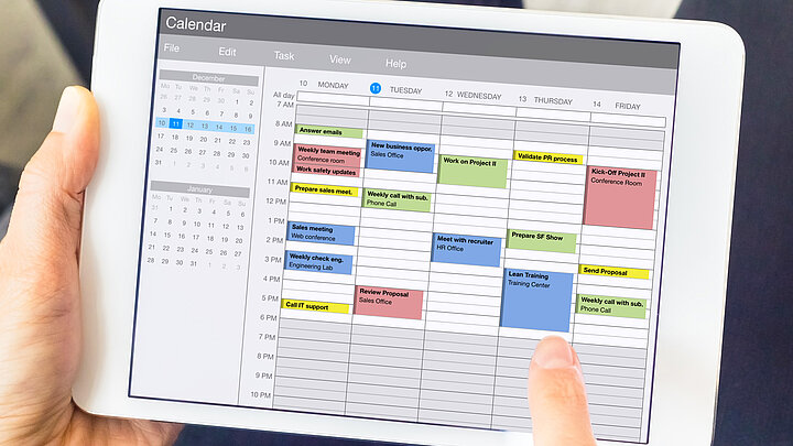 Grafika dekoracyjna. Tablet z wyświetlonym kalendarzem, z zaznaczonymi na kolorowo zadaniami do wykonania. 